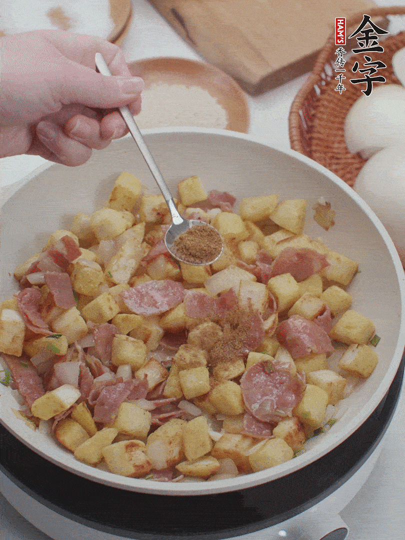 起鍋少油，煸香洋蔥丁、蔥白，加入金字培根火腿翻炒幾下，再加入饅頭丁、1小勺孜然粉、少許鹽翻炒均勻并鋪平。